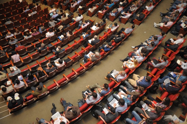 Publikumsbereich eines Hörsaals die roten Sitze sind zu etwa zwei Drittel besetzt.