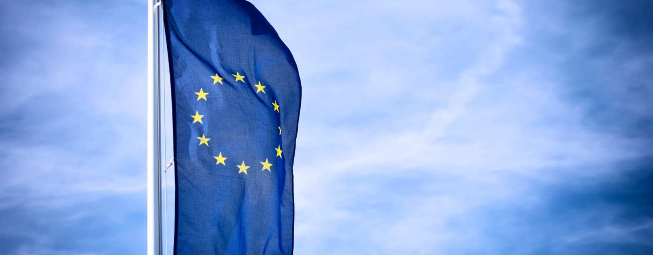 Eine blaue Fahne mit gelben Sternen, die Flagge der EU, weht vor einem blauen Himmel.