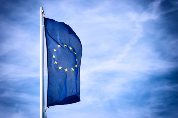 Eine blaue Fahne mit gelben Sternen, die Flagge der EU, weht vor einem blauen Himmel.