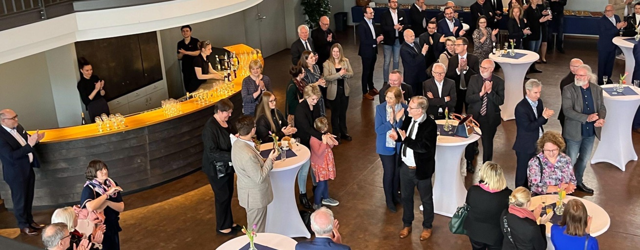 Gäste der Feier zur Emeritierung von Prof. Stephan Weth stehen in der Aula der Universität des Saarlandes. Dazwischen Stehtische. Im Hinergrund eine Bar, an der Getränke ausgeschenkt werden.